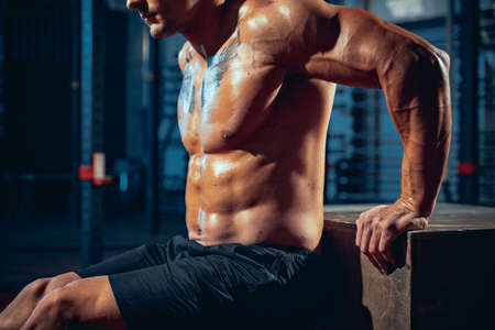 Cropped shot of muscled athlete, bodybuilder workouts alone at sport gym, indoors. Concept of sport,...