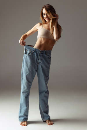 Portrait of young beautiful slim woman in blue jeans jumpersuit posing isolated over gray studio background. Weight Loss concept.の写真素材