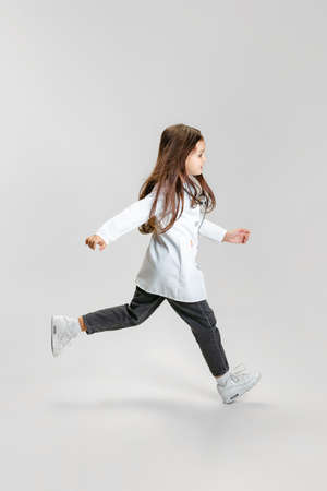 Full-length portrait of cute beautiful little girl, child in image of doctor wearing white lab coat...