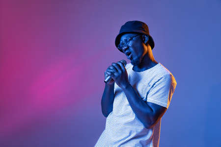 Studio shot of emotive african man with microphone isolated over gradient purple pink color studio background in neon filterの写真素材