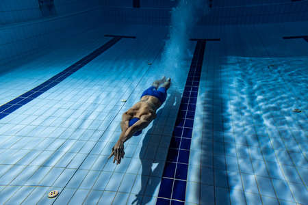 Underwater shooting. One male swimmer training at pool, indoors. Underwater view of swimming movements details.の写真素材