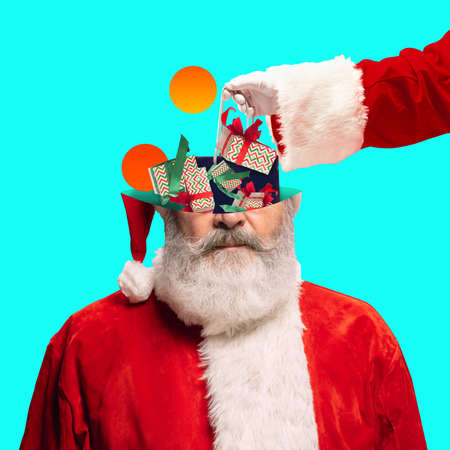 Contemporary art collage. Santa Clauss head and gifts, boxes isoalted on blue background. Happy New Year and Merry Christmas 2022の写真素材