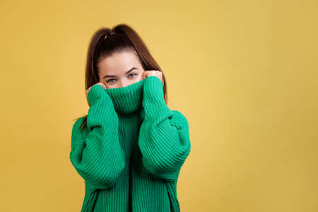 Half-lenght portrait of young cute girl, student wearing green sweater posing isolated on yellow studio background. Concept of emotions, fashionの写真素材