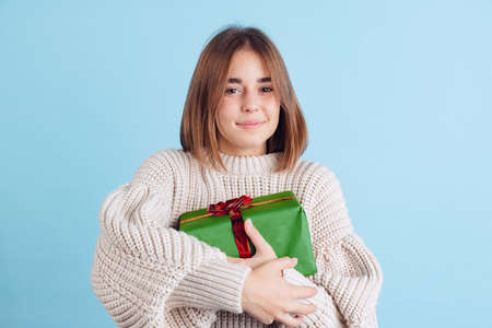 Portrait of young girl, teen or student in casual clothes holding New Year gift box isolated on blue...