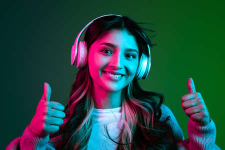 Studio shot of young adorable cute girl, student in casual style clothes posing isolated on dark green studio backgroud in pink neon light.の写真素材