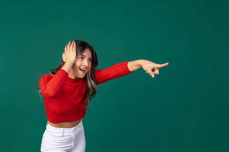 Dynamic portrait of young beuatiful girl, student in bright red sweater pointing at isolated on...