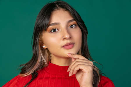 Close-up portrait of young beuatiful girl, student in bright red sweater isolated on green studio...