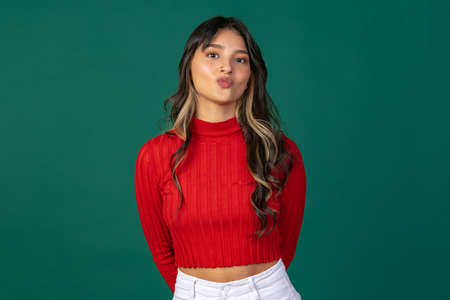 Close-up portrait of young beuatiful girl, student in bright red sweater isolated on green studio backgroud.の写真素材