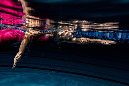 Close-up female swimmer in swimming cap and goggles training at pool, indoors. Underwater view of swimming movements details.の写真素材