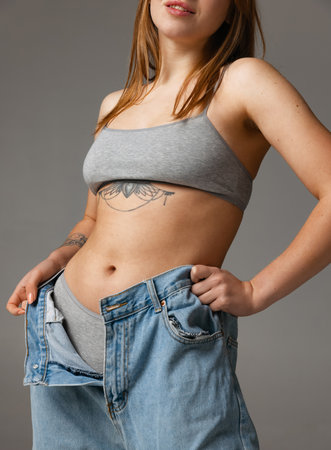 Cropped portrait of young beautiful slim woman in blue jeans jumpersuit posing isolated over gray studio background. Weight Loss concept.の写真素材