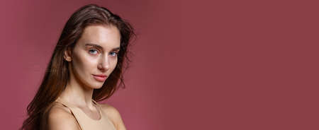 Close-up portrait of young beautiful girl without makeup isolated over dark pink studio background....