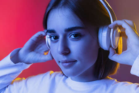 Close-up portrait of young cute girl, student in casual clothes listening to music isolated on...