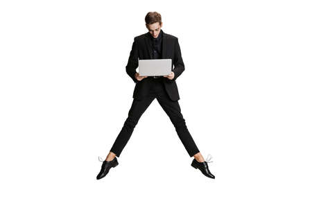 One handsome man in black business suit flying and using laptop isolated on white background. Art, inspiration concept.の写真素材
