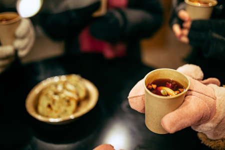 Close-up human hands in winter mittens with hot cup of hot mulled wine with spices. Holidays, traditions, winter fair, Christmas conceptの写真素材