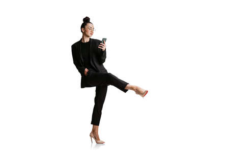 Studio shot of young woman in business style attire using phone isolated on white background. Art,...