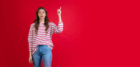 Emotional young beautiful girl in sweater and jeans posing isolated on red studio background. Concept of emotions, facial expressionの写真素材