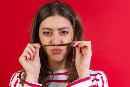 Emotional young beautiful girl in sweater and jeans posing isolated on red studio background....