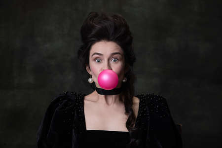 Close-up classic retro portrait of young cute woman in image of medieval royal person having fun isolated on dark vintage background.の写真素材