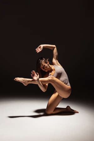 Dynamic portrait of young flexible contemp dancer dancing isolated on dark studio background in spotlight. Art, beauty, inspiration concept.の写真素材