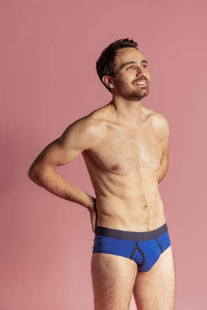 Half-length portrait of young handsome bearded shirtless man standing alone isolated on pink studio background.の写真素材
