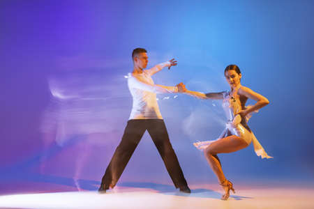 Two young graceful dancers, flexible man and woman dancing ballroom dance isolated on gradient blue...