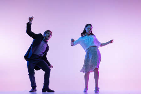 Dynamic portrait of young dancers, man and woman in vintage style outfits dancing swing isolated on lilac color background in neon lightの写真素材