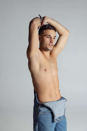 Portrait of young handsome sportive shirtless man in jeans posing isolated on gray studio background.の写真素材