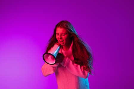 Portrait of young pretty girl shouting at megaphone isolated over purple studio background in neon...