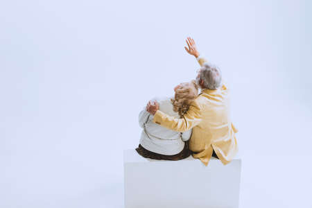 Back view of two people, senior woman and bearded man in retro style clothes, fashion of 70s, 60s years sitting together isolated on white studio backgroundの写真素材