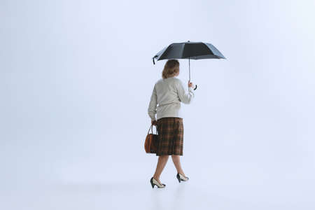 Portrait of senior sad woman in retro style, fashion of 70s, 60s years walking with umbrella isolated on white studio backgroundの写真素材