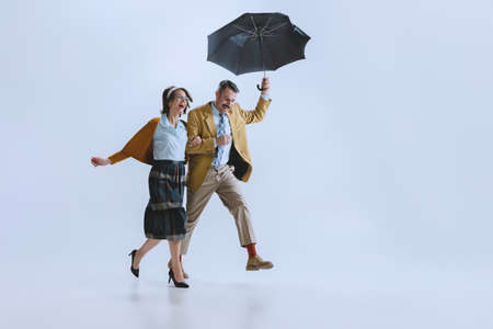Young happy family couple, man and woman in retro style clothes, fashion of 70s, 60s years walking with umbrella isolated on white studio backgroundの写真素材