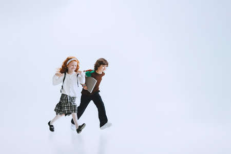 Two kids, school boy and girl running isolated on white studio background. Childhood, dreams,...