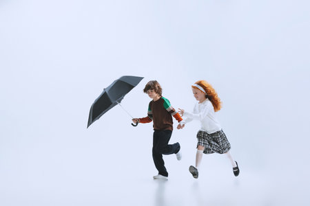 Two happy kids, boy and girl running with umbrella isolated on white studio background. Childhood, dreams, imagination, educationの写真素材