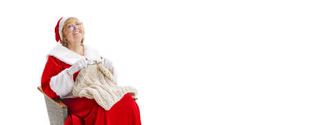 Flyer with happy smiling beautiful middle-age woman in Christmas costume sitting at armchair and knits sweater isolated on white background.の写真素材