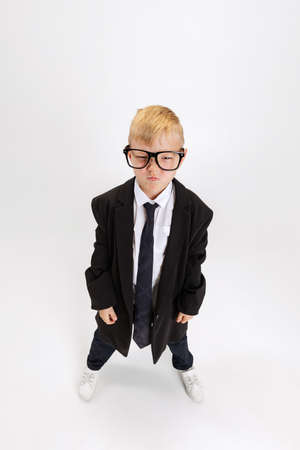 High angle view of cute little boy, kid businessman in huge suit jacket wearing eyeglasses isolated on white studio background.の写真素材