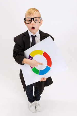 High angle view of cute little boy, kid businessman in huge suit jacket wearing eyeglasses isolated on white studio background.の写真素材