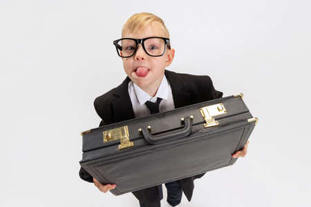 Close-up of cute little boy, kid businessman in huge fathers suit holding big vintage attache case...