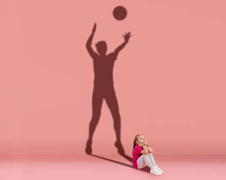 Conceptual image with kid and shadow of female volleyball player on studio wall. Dreams about sport...