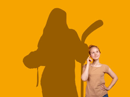 Conceptual image with young girl dreaming about future sport career. Shadow of strong female hockey player on yellow wallの写真素材