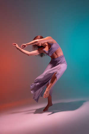 Portrait of young flexible contemp dancer in lilac color stage attire dancing isolated on gradient...