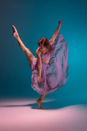Young adorable flexible contemp dancer in lilac dress dancing isolated on gradient blue white background in neon.の写真素材
