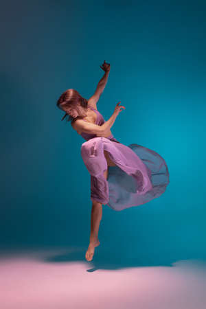 One young flexible contemp dancer in lilac dress dancing isolated on gradient blue white background in neon.の写真素材