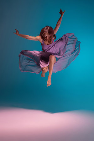 One young flexible contemp dancer in lilac dress dancing isolated on gradient blue white background in neon.の写真素材