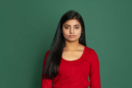 Close-up young beautiful serious girl, student looking at camera isolated on dark green studio backgroudの写真素材