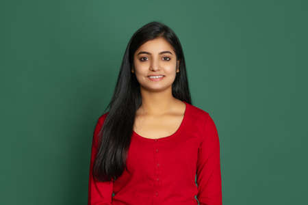 Half-length portrait of young beautiful smiling girl, student looking at camera isolated on dark green studio backgroudの写真素材