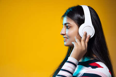 Profile view of young girl with long black hair listening to music in headphones isolated on yellow color studio backgroundの写真素材