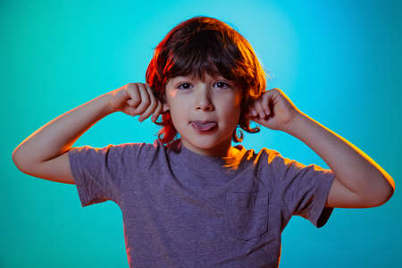 Portrait of little boy, curly smiling kid having fun isolated on blue studio background in neon light, filter.の写真素材