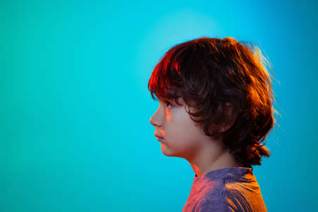 Profile view of little boy, curly kid posing isolated on blue studio background in neon light, filter.の写真素材