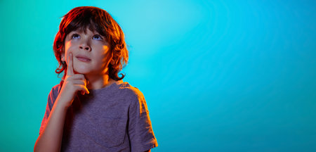 Flyer with portrait of little boy, kid raising finger up isolated on blue studio background in neon light, filter.の写真素材