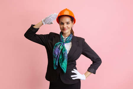Happy young girl, female flight attendant in orange color protective helmet posing isolated on pink studio background.の写真素材